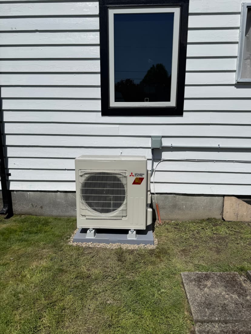 Mitsubishi outdoor air conditioning unit installed beside a white house.